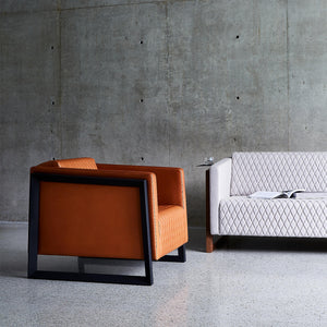 A pair of modern designer armchairs sit side by side on a concrete floor in tan leather and soft grey wool finishes